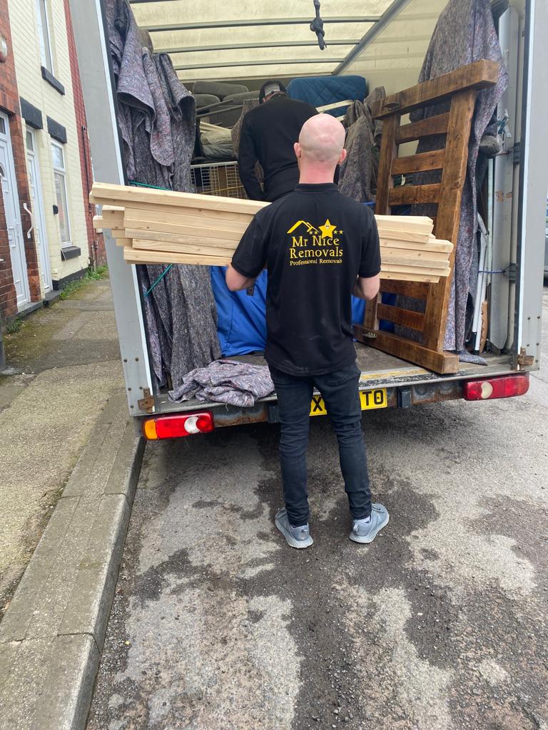 A man standing in the back of a truck with wood.